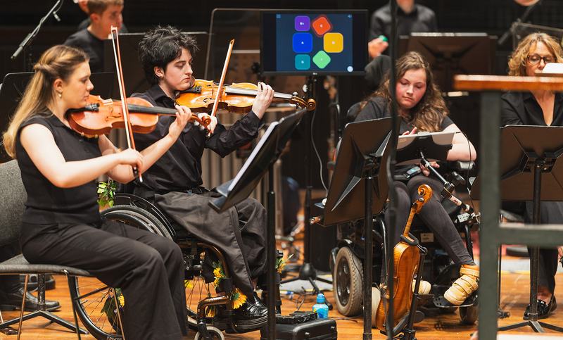 National Open Youth Orchestra musicians at a performance, sat with their instruments.